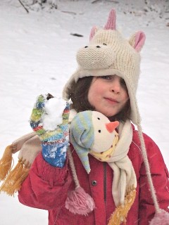 Phoebe in a unicorn hat, holding a snowball.